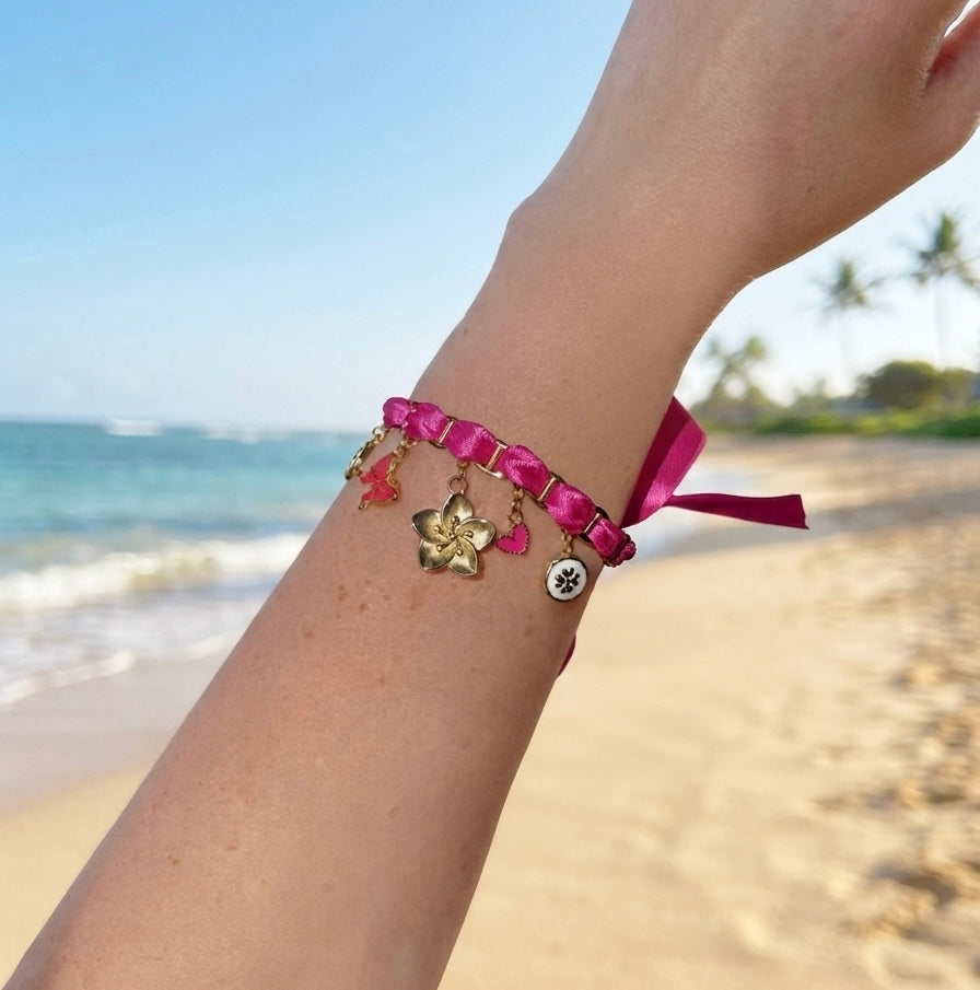 Détail des breloques du bracelet fuchsia blanc : médaillons émaillés, papillon, fleur et cœur dorés
