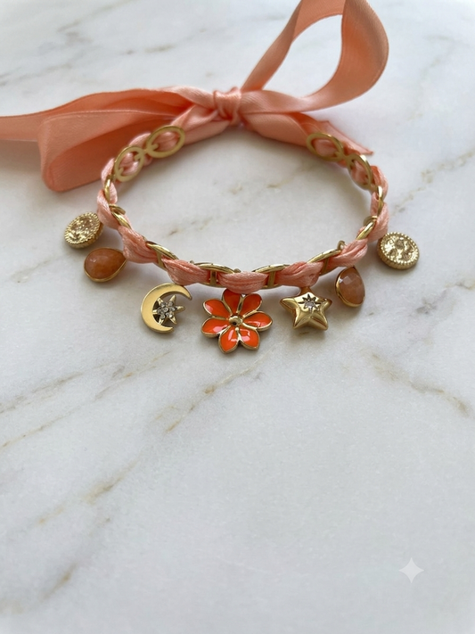 Bracelet saumon en acier inoxydable porté au poignet avec breloques dorées fleur et lune