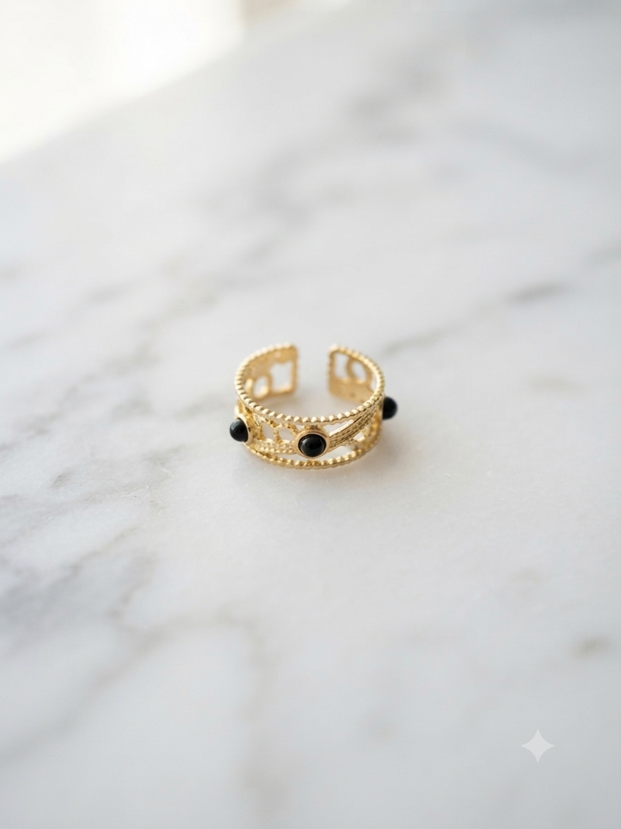 Bague Nymphe ajourée aux perles noires, posée sur fond marbre blanc