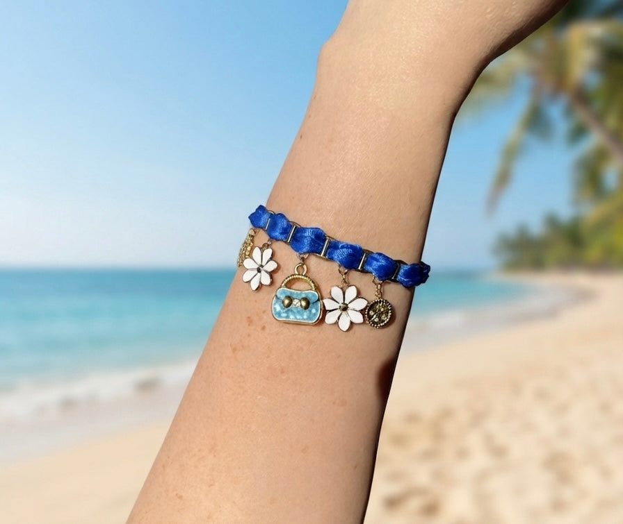 Détail des breloques du bracelet bleu électrique : médaillons dorés, fleurs blanches et sac émaillé