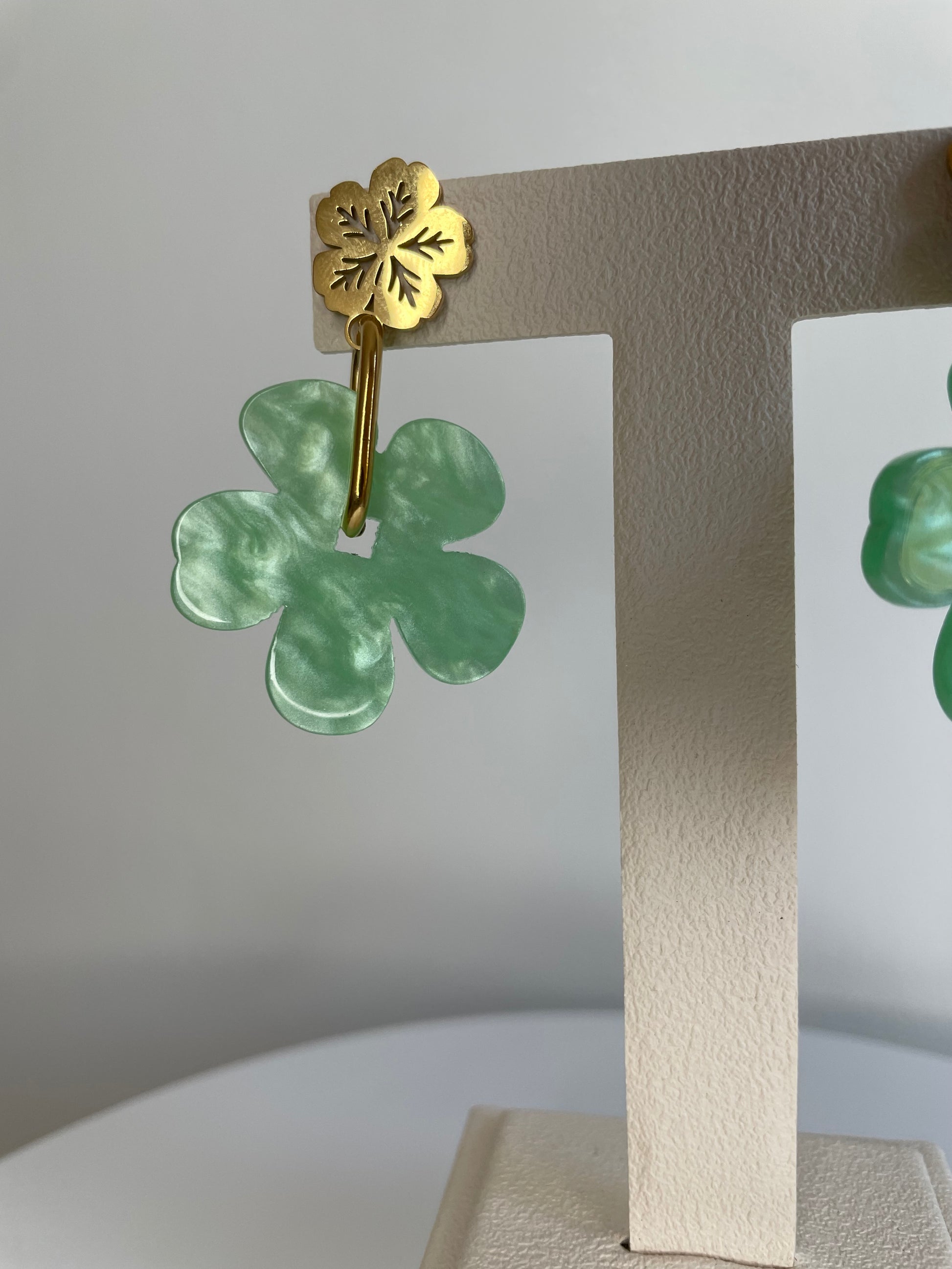 Gros plan sur la boucle d'oreille Sola, puce fleur dorée et fleur vert marbré
